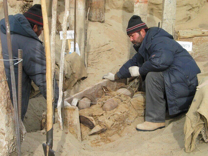 两个穿着厚夹克的人在挖掘一座坟墓